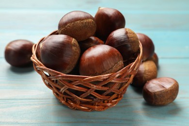 Photo of Wicker bowl with roasted edible sweet chestnuts on light blue wooden table, closeup