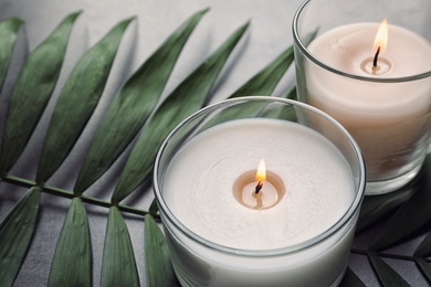 Burning wax candles and tropic leaf on table