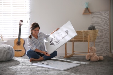 Photo of Decorator with pictures on floor in baby room. Interior design