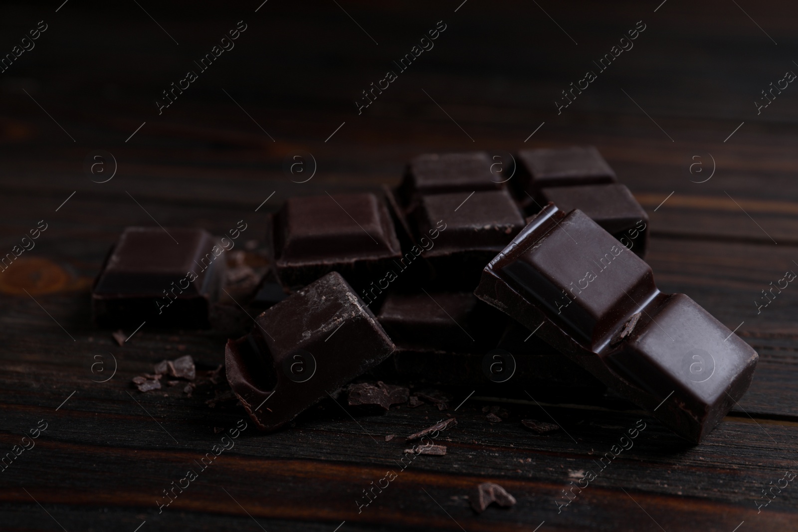 Photo of Pieces of delicious dark chocolate on wooden table