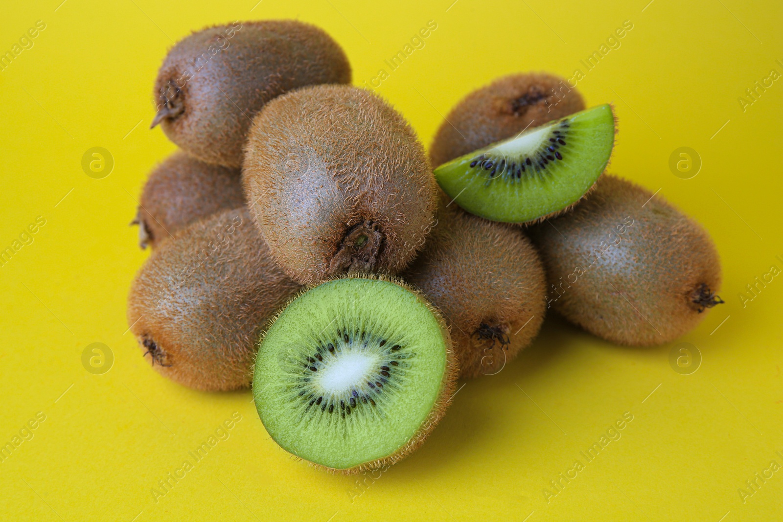 Photo of Heap of whole and cut fresh kiwis on yellow background