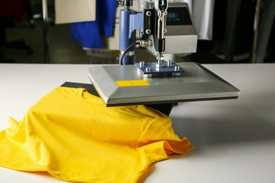 Photo of Printing logo. Heat press with yellow t-shirt on white table