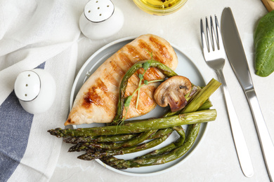 Tasty grilled chicken fillet served with asparagus on light grey marble table, flat lay