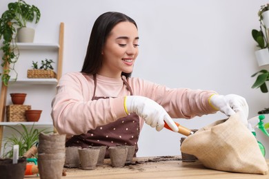 Photo of Woman filling pots with soil at wooden table indoors. Growing vegetable seeds