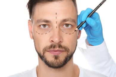 Photo of Doctor marking mature man face before cosmetic surgery on white background
