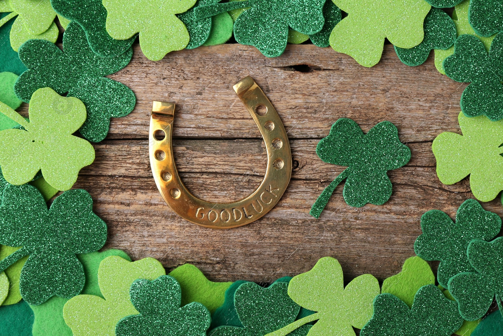 Photo of St. Patrick's day. Golden horseshoe and green decorative clover leaves on wooden table, flat lay