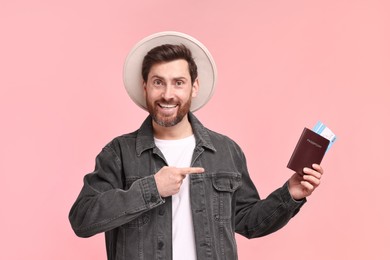 Photo of Smiling man pointing at passport and tickets on pink background