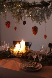 Christmas celebration. Cones hanging from fir tree branch over table with burning candles and tableware