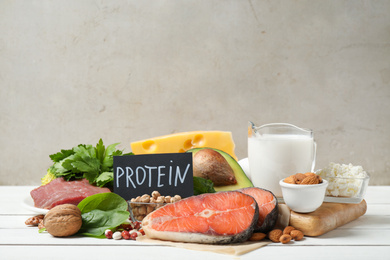 Photo of Card with word PROTEIN and different products on white wooden table