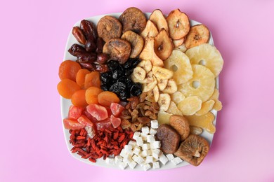 Photo of Plate with different dried fruits on violet background, top view