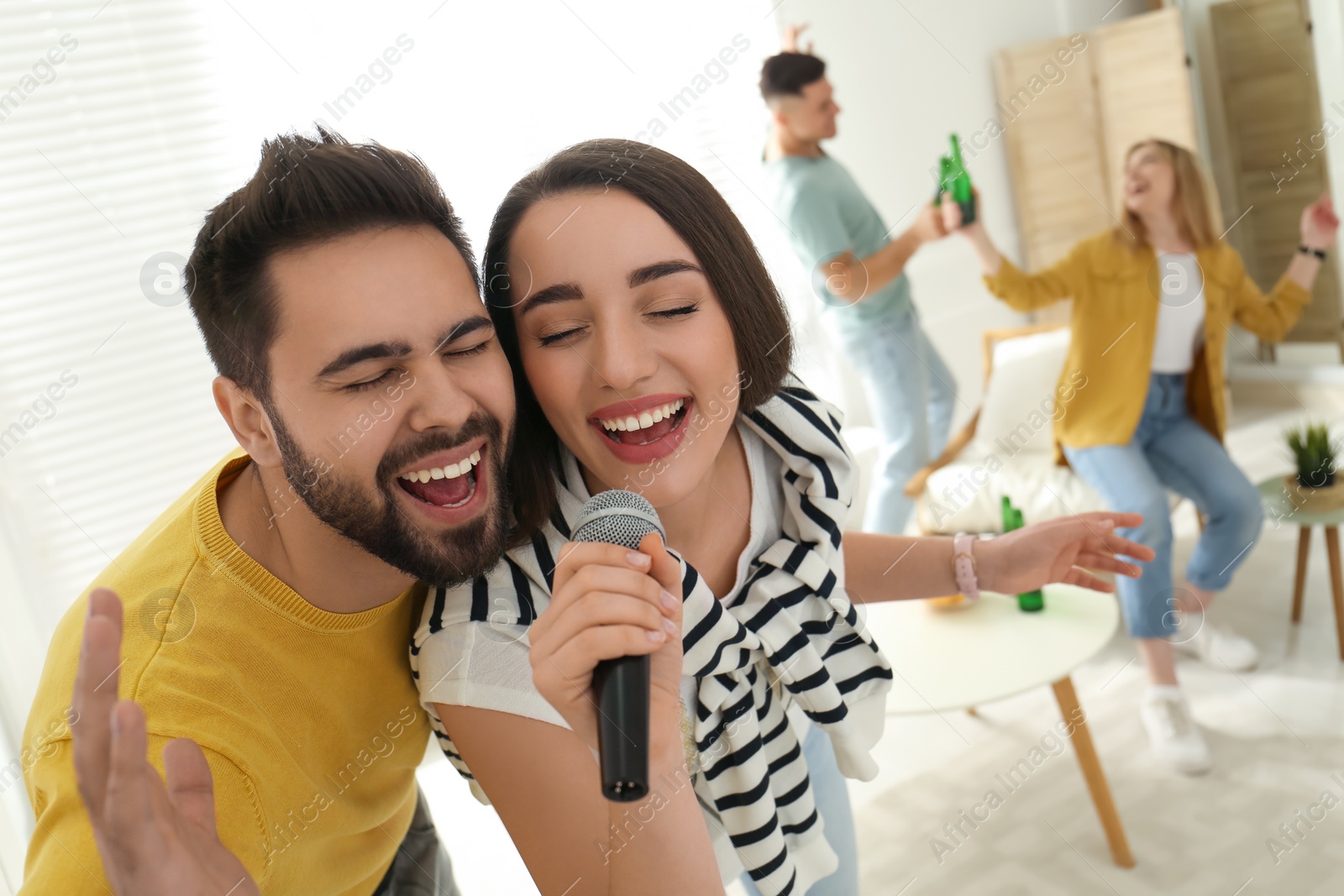 Photo of Happy couple singing karaoke with friends at home