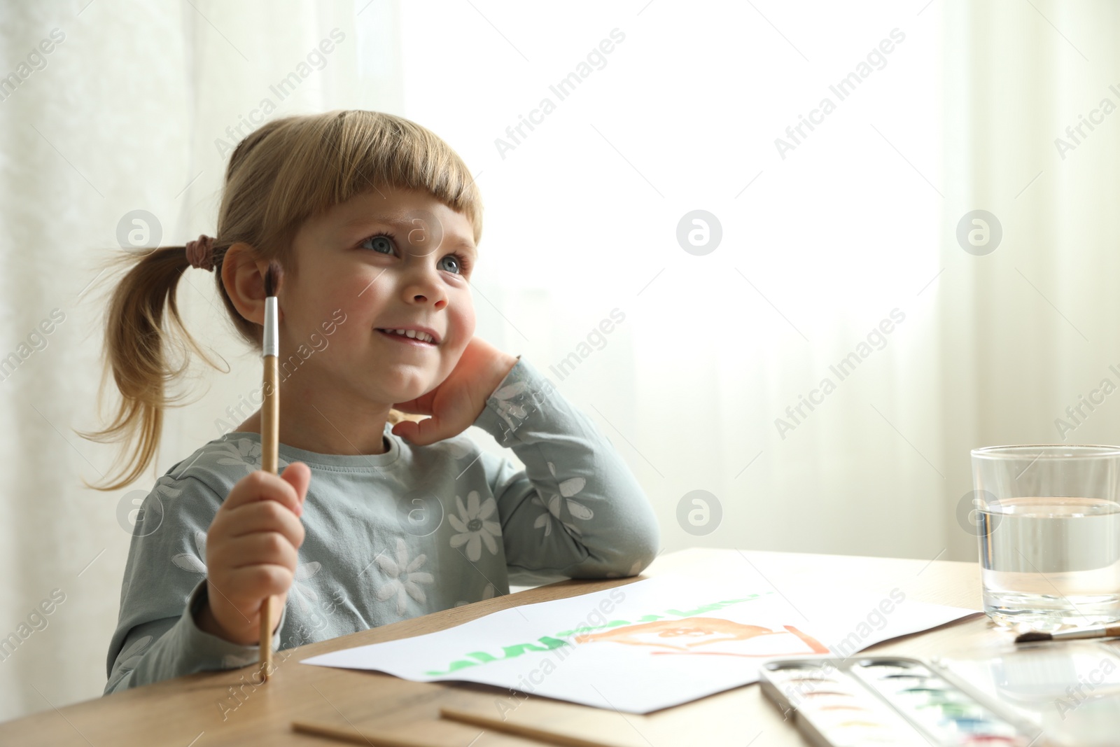 Photo of Cute little girl drawing at wooden table indoors. Child`s art