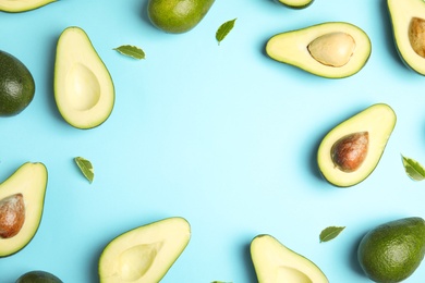 Frame of ripe avocados and leaves on blue background, flat lay with space for text