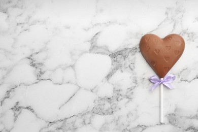 Photo of Chocolate heart shaped lollipop on white marble table, top view. Space for text