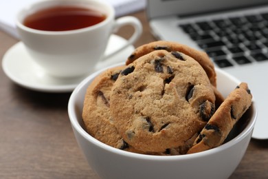 Chocolate chip cookies near laptop and cup of tea on table, closeup