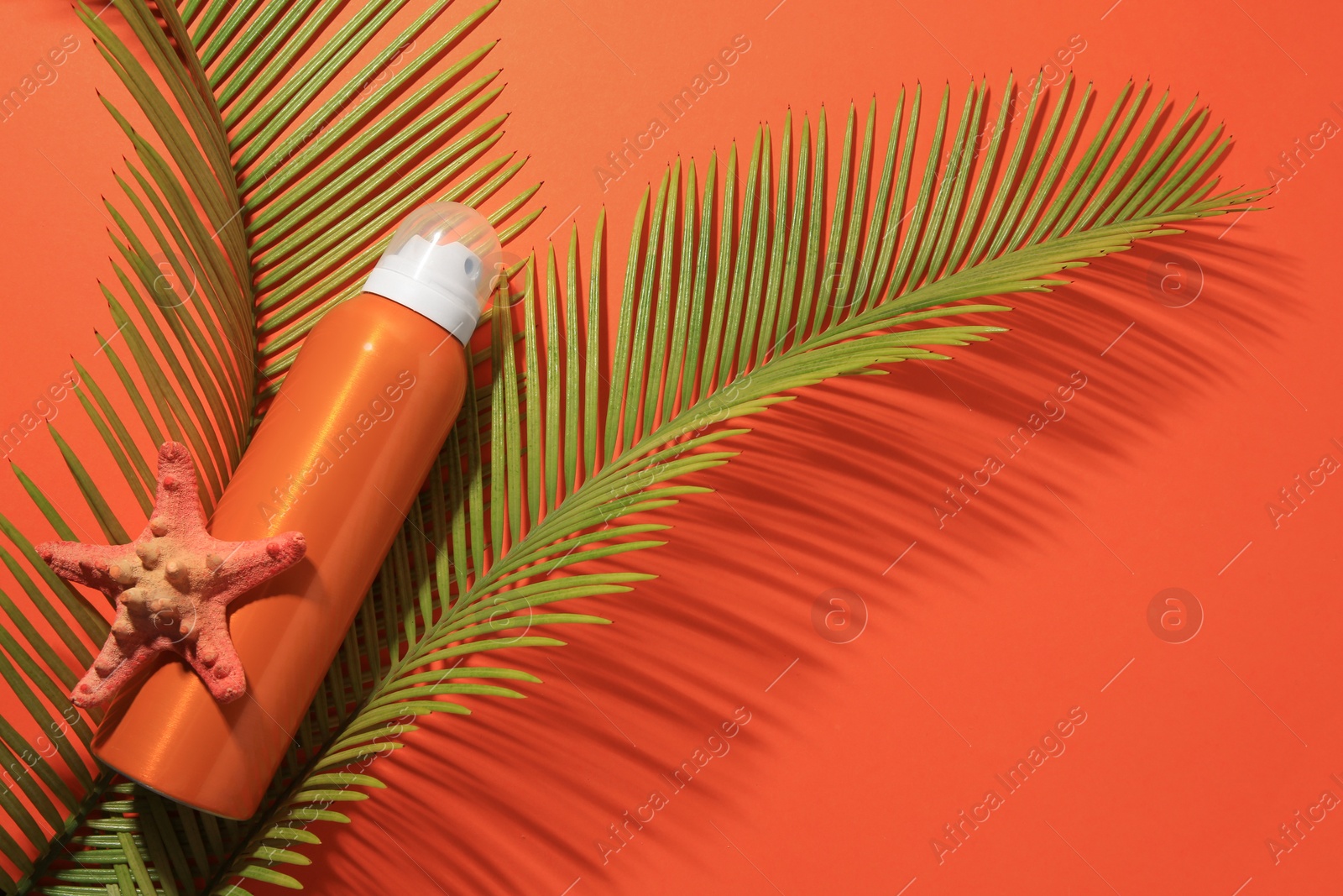 Photo of Sunscreen, starfish and tropical leaves on coral background, flat lay and space for text. Sun protection care