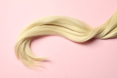 Photo of Blonde hair strand on pink background, top view