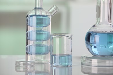 Laboratory analysis. Different glassware with liquid on white table against blurred background, closeup