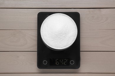 Photo of Electronic scales with sugar on light wooden table, top view