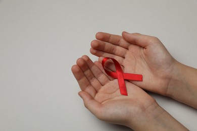 Photo of Little girl holding red ribbon on beige background, closeup with space for text. AIDS disease awareness