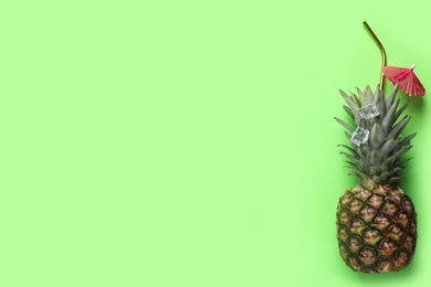 Photo of Creative composition with pineapple, ice, straw and cocktail umbrella on green background. Space for text