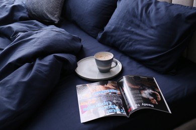 Photo of Open magazine and cup of coffee on bed with stylish silky linens