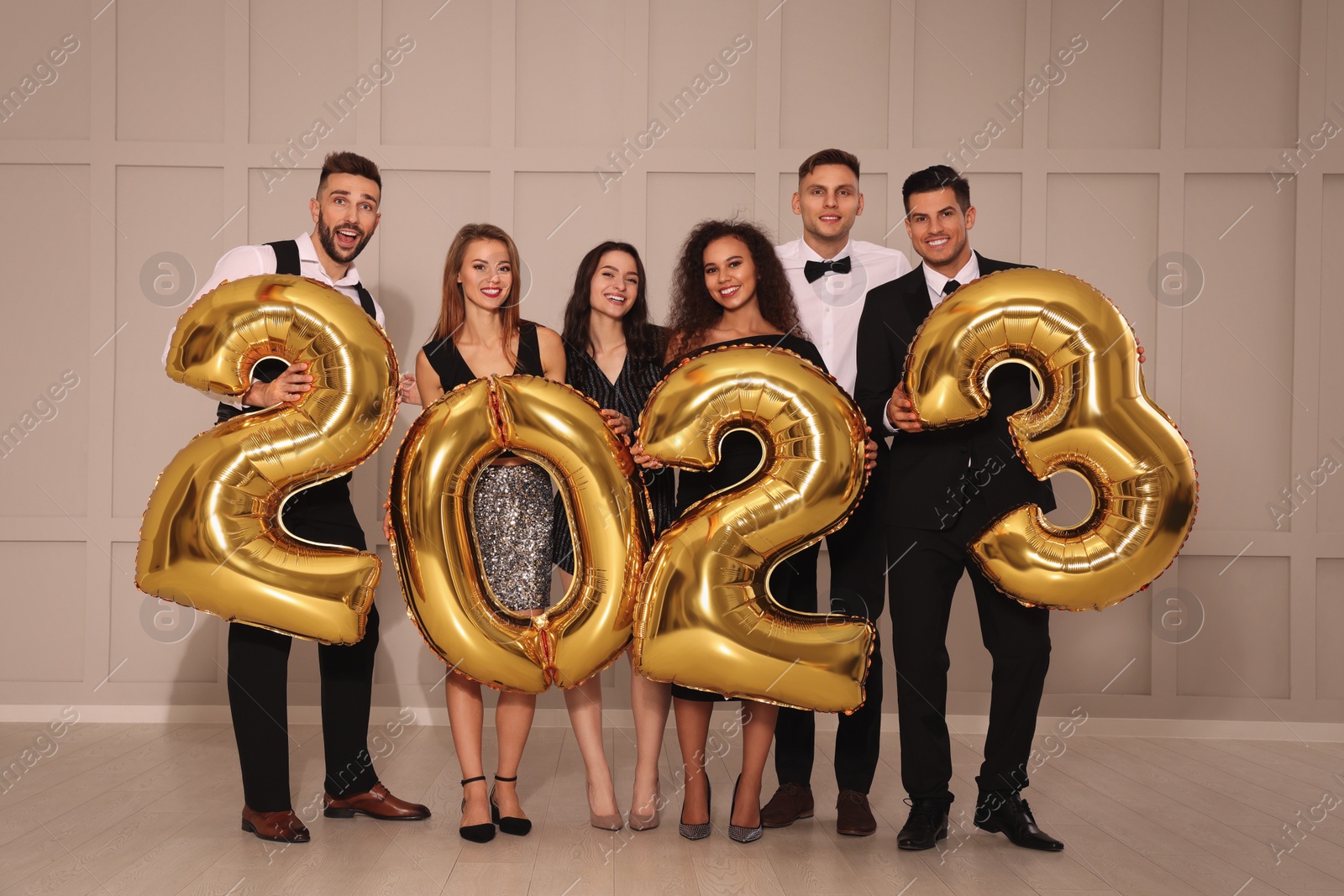 Photo of Happy friends with golden 2023 balloons indoors. New Year celebration