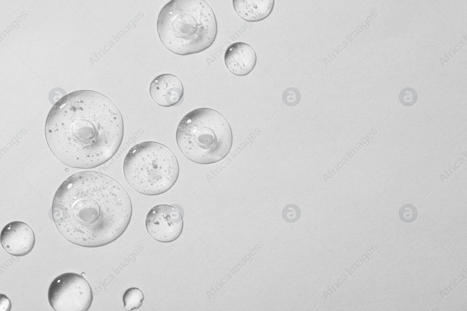 Photo of Drops of cosmetic serum on white background, top view. Space for text