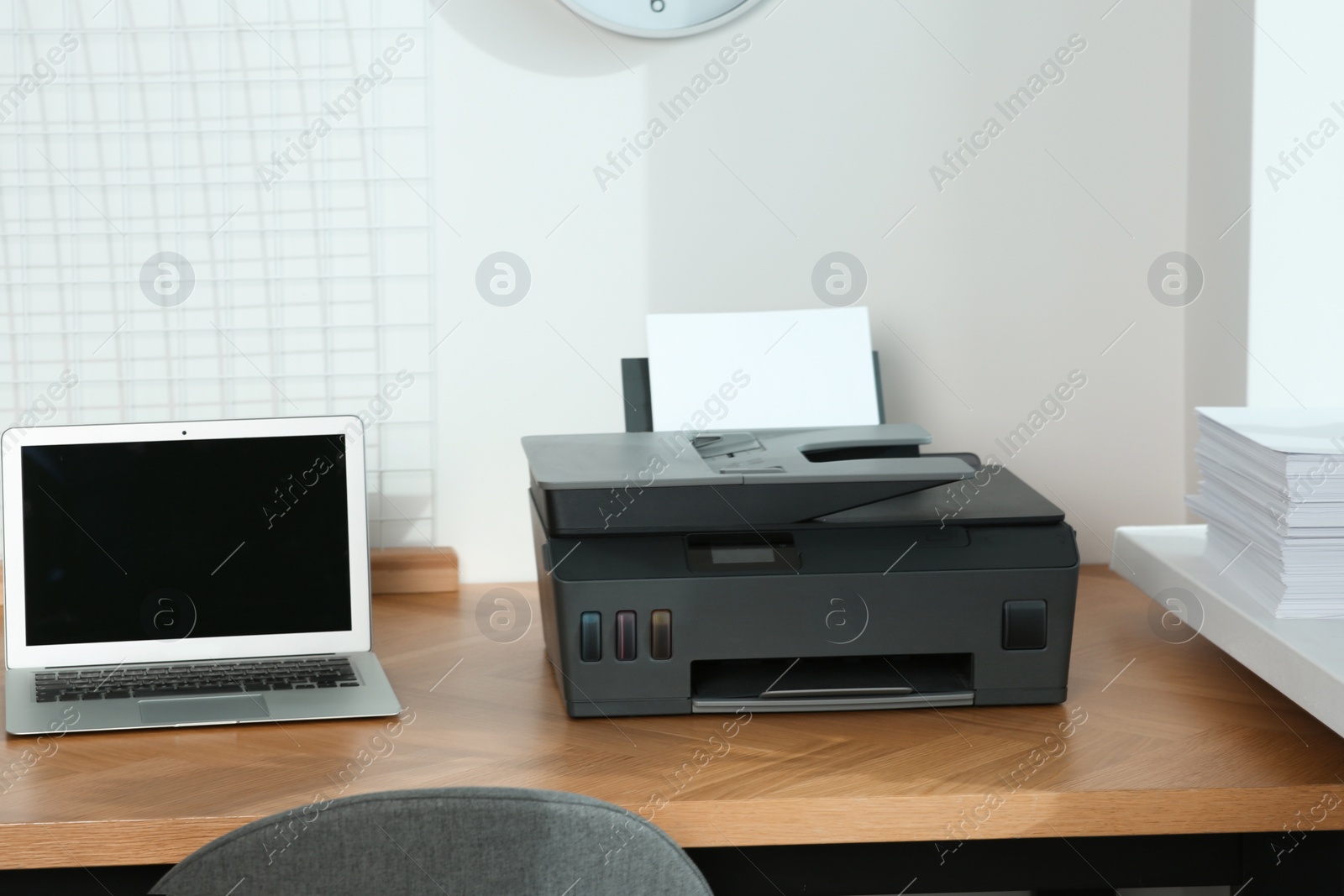 Photo of Modern printer with paper and laptop on wooden table in office