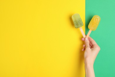 Photo of Woman holding delicious ice pops on color background, top view with space for text. Fruit popsicle