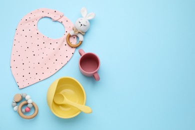 Flat lay composition with baby feeding accessories and bib on light blue background, space for text