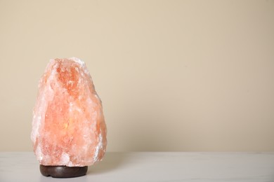 Photo of Himalayan salt lamp on table against beige wall. Space for text