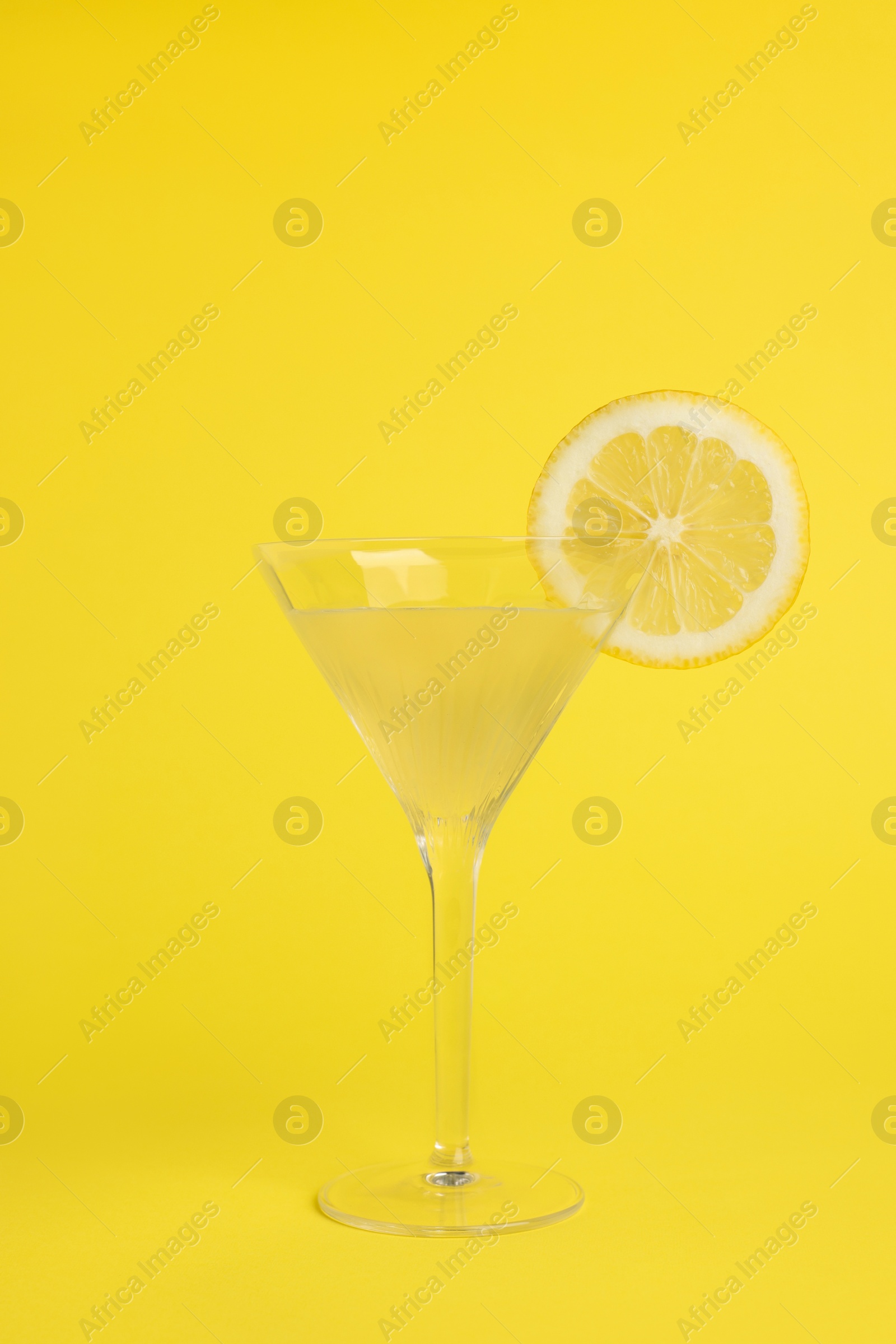 Photo of Martini glass of refreshing cocktail with lemon slice on yellow background