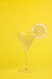 Photo of Martini glass of refreshing cocktail with lemon slice on yellow background