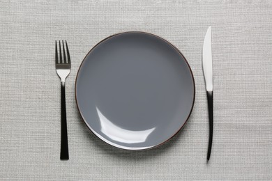 Photo of Clean plate and shiny silver cutlery on grey tablecloth, flat lay