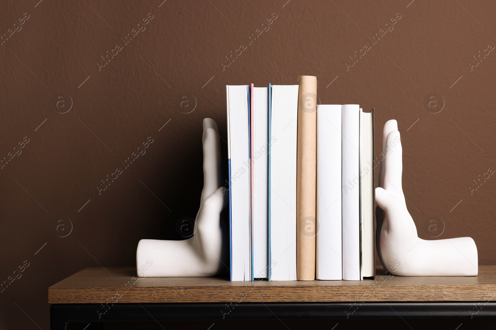 Photo of Beautiful hand shaped bookends with books on shelf near brown wall
