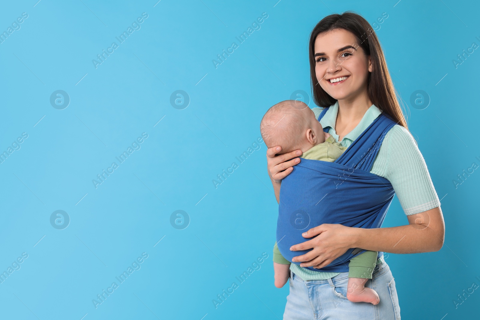 Photo of Mother holding her child in sling (baby carrier) on light blue background. Space for text