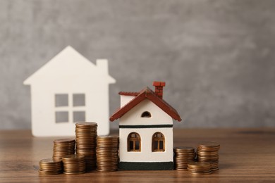 Photo of House models and stacked coins on wooden table against gray background, space for text