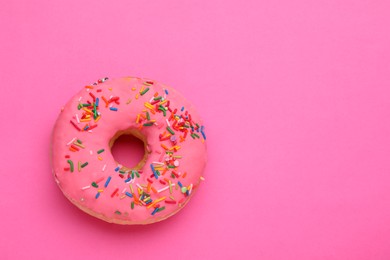 Photo of Sweet glazed donut decorated with sprinkles on pink background, top view and space for text. Tasty confectionery