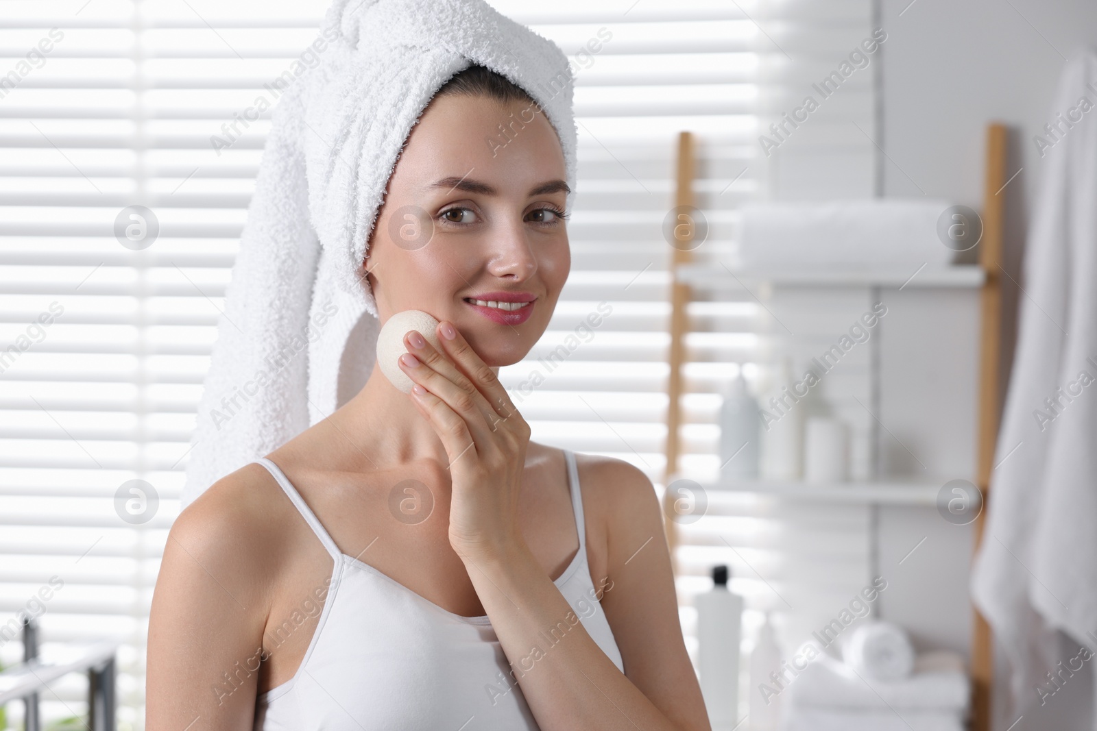 Photo of Happy young woman washing her face with sponge in bathroom. Space for text