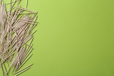 Wooden toothpicks on green background, flat lay. Space for text