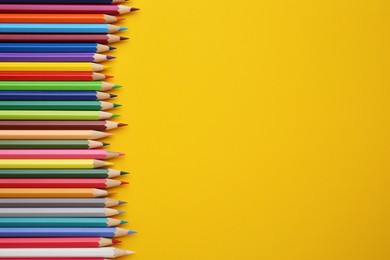 Colorful wooden pencils on yellow background, flat lay. Space for text