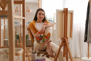 Photo of Beautiful young woman with drawing tools near easel at home