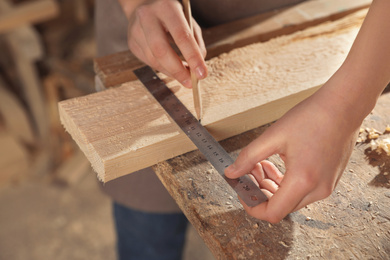 Professional carpenter measuring wooden plank in workshop, closeup