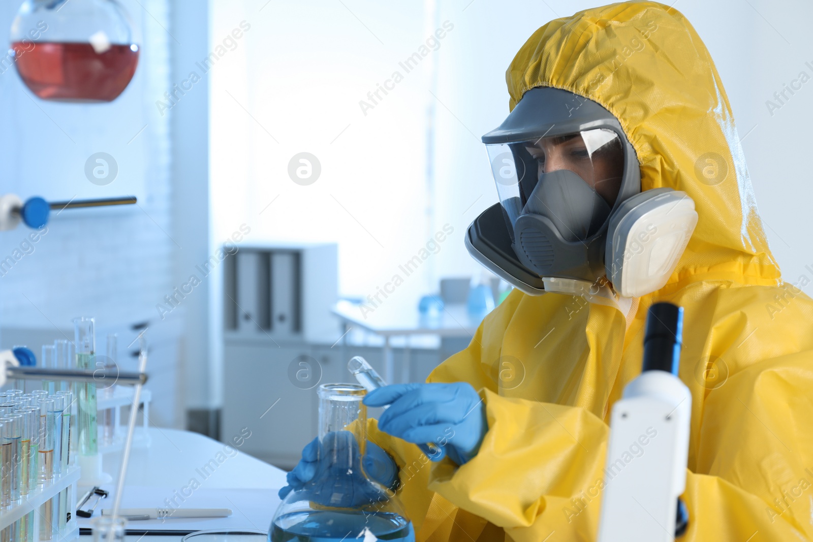 Photo of Scientist in chemical protective suit pouring reagent into flask at laboratory. Virus research