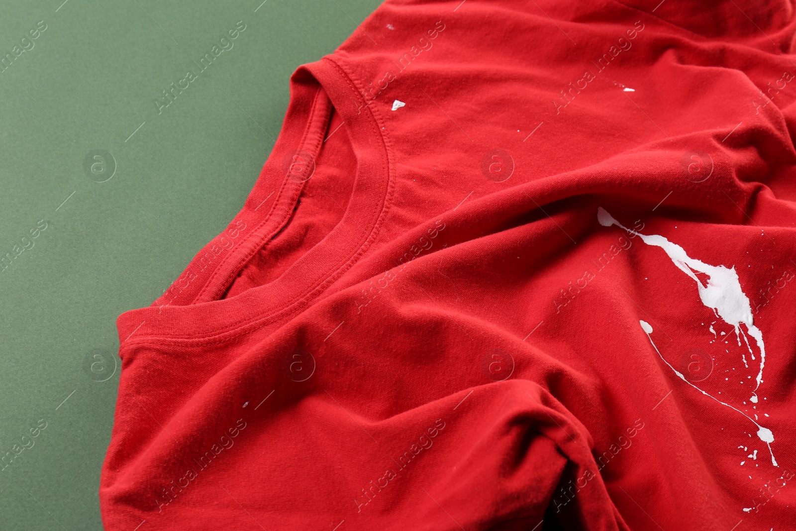 Photo of Red shirt with white paint stain on green background, above view