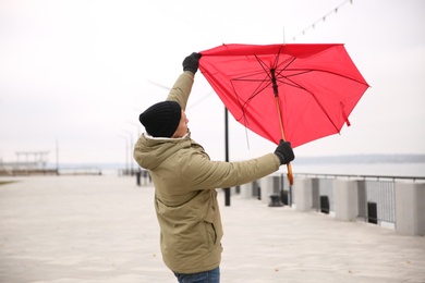 Photo of Man with red umbrella caught in gust of wind outdoors