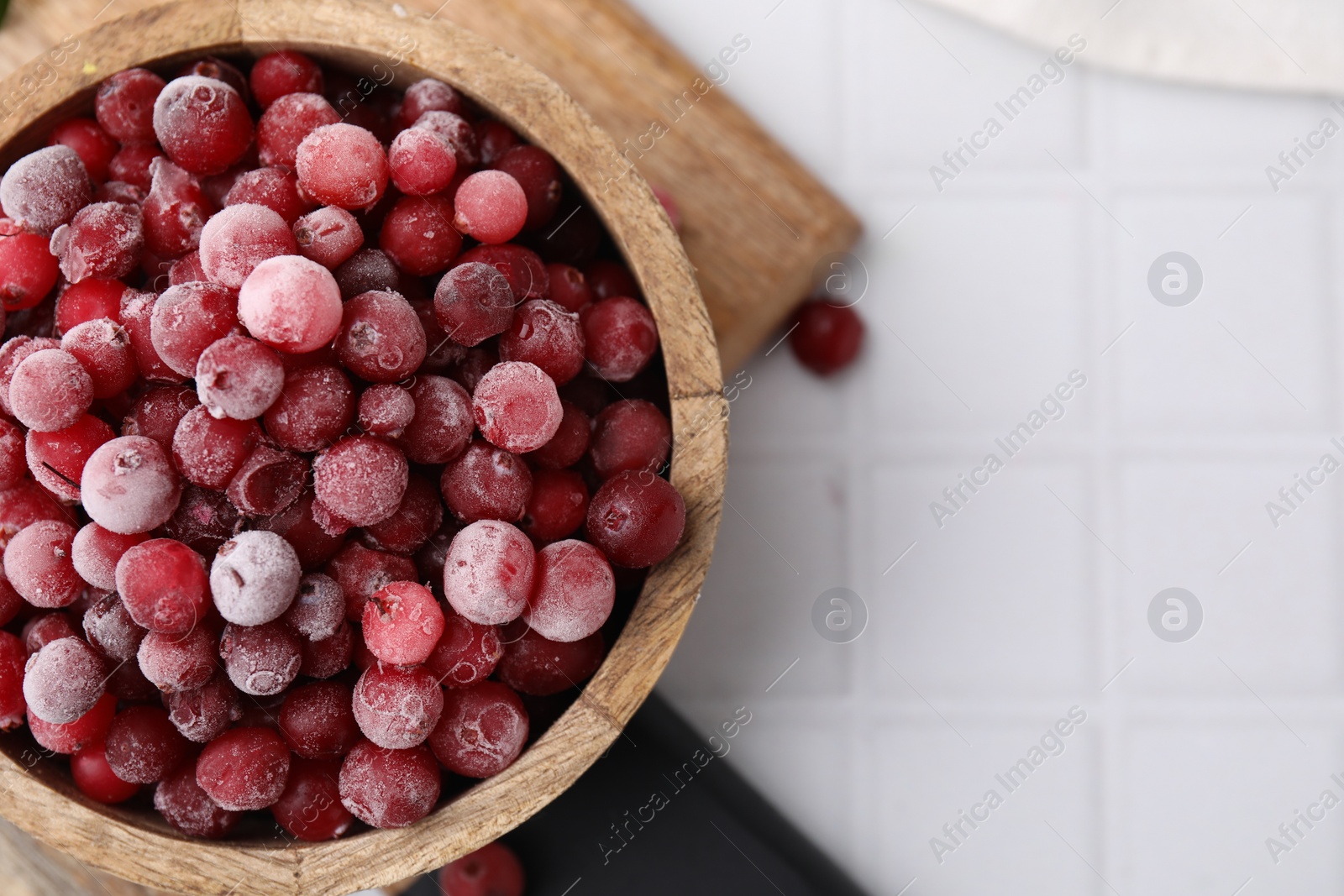 Photo of Frozen red cranberries in bowl on white tiled table, top view. Space for text