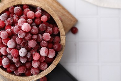 Photo of Frozen red cranberries in bowl on white tiled table, top view. Space for text