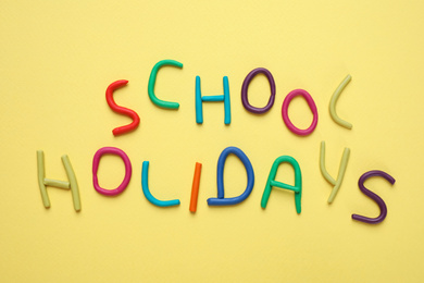 Phrase School Holidays made of modeling clay on yellow background, top view